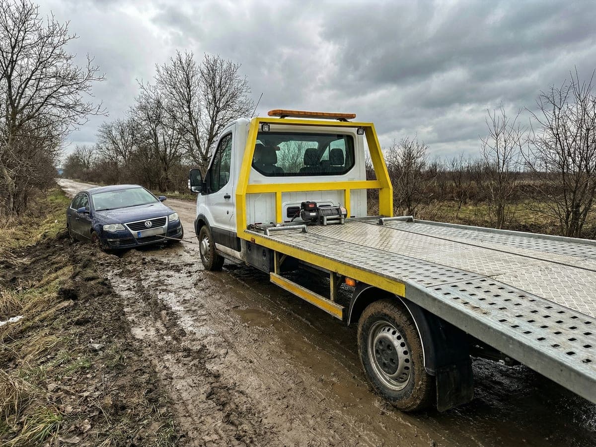 Platforma de tractare scoțând o mașină din noroi de pe drum rural